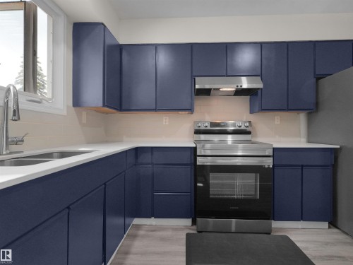 Kitchen featuring blue cabinetry, white countertops, stainless steel appliances, and a tile backsplash - #47 1904 48 St Nw, Edmonton, AB - Indoor Photo Showing Kitchen With Double Sink