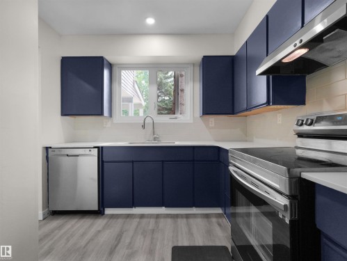 Kitchen featuring navy cabinetry, white countertops, stainless steel appliances, a white subway tile backsplash, and wood-finish flooring - #47 1904 48 St Nw, Edmonton, AB - Indoor Photo Showing Kitchen