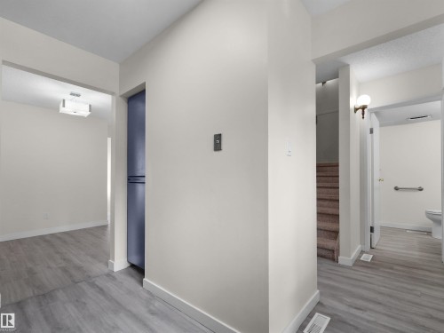 Light grey wood-finish flooring, built-in storage cabinet, carpeted stairs, wall-mounted light fixture, and grab bar in bathroom - #47 1904 48 St Nw, Edmonton, AB - Indoor Photo Showing Other Room