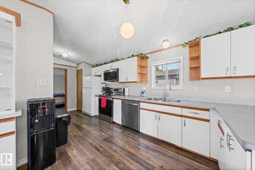 Kitchen featuring wood-finish flooring, white cabinetry, integrated stainless-steel appliances, and a double basin sink - 89 Springfield Crescent, Spruce Grove, AB 