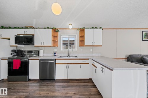 Kitchen featuring white cabinetry, stainless steel appliances, wood-finish flooring, a double basin sink, and a breakfast bar - 89 Springfield Crescent, Spruce Grove, AB 