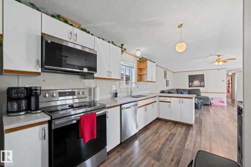 Kitchen featuring white cabinetry, stainless steel appliances, a corner sink, wood-finish flooring, and a ceiling-mounted light fixture - 89 Springfield Crescent, Spruce Grove, AB 