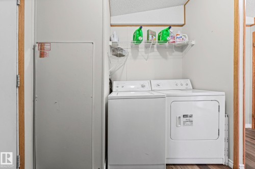 Dedicated laundry room featuring side-by-side washer and dryer appliances, wall-mounted shelving with storage, large mirror, and wood-trimmed doorway - 89 Springfield Crescent, Spruce Grove, AB 