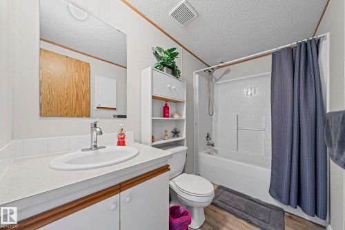 Vanity with an oval sink and chrome faucet, wood-finish flooring, white tub and shower combination, built-in shelving, and a wall-mounted mirror - 89 Springfield Crescent, Spruce Grove, AB 
