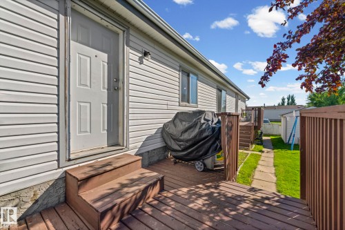 Rear exterior featuring white horizontal siding and a wood-finish deck with railing - 89 Springfield Crescent, Spruce Grove, AB 