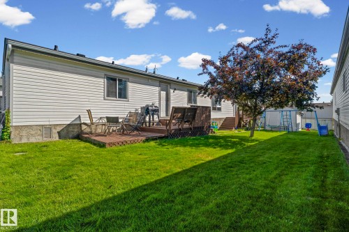 Expansive backyard featuring a manicured lawn, a mature tree, and a multi-level wooden deck - 89 Springfield Crescent, Spruce Grove, AB 