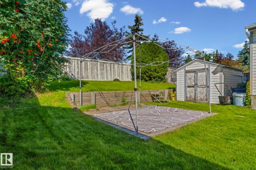 Expansive green lawn, wood fence, concrete patio, garden shed, mature trees, and a tiered landscape design - 89 Springfield Crescent, Spruce Grove, AB 