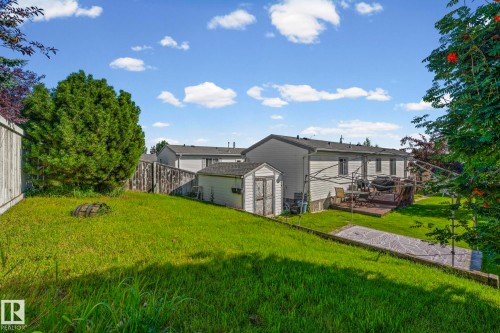 Expansive backyard featuring a manicured lawn, established trees, a wood deck, a storage shed, and a privacy fence - 89 Springfield Crescent, Spruce Grove, AB 