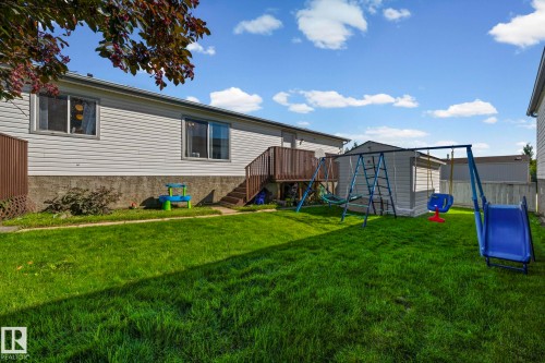 Expansive backyard featuring a manicured lawn, mature tree canopy, and recreational play equipment - 89 Springfield Crescent, Spruce Grove, AB 