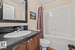 White oval basin with a chrome faucet, dark countertop, and wood-finish vanity cabinetry - 