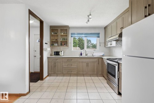 Kitchen featuring wood-finish cabinetry, stainless steel oven, white tile flooring, white countertops, and a window with a blue roller shade - 10007 168 Avenue Nw, Edmonton, AB - Indoor Photo Showing Kitchen