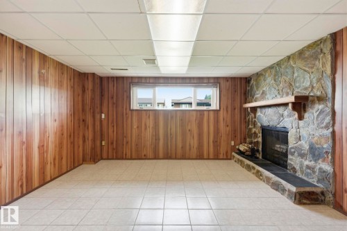 Stone fireplace with a wood mantle, wood paneling, tiled flooring, and a drop ceiling with fluorescent lighting - 10007 168 Avenue Nw, Edmonton, AB - Indoor Photo Showing Other Room With Fireplace