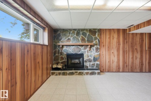 Stone-clad fireplace with a wood mantle, wood paneling, white window frame, and tiled flooring - 10007 168 Avenue Nw, Edmonton, AB - Indoor Photo Showing Other Room With Fireplace