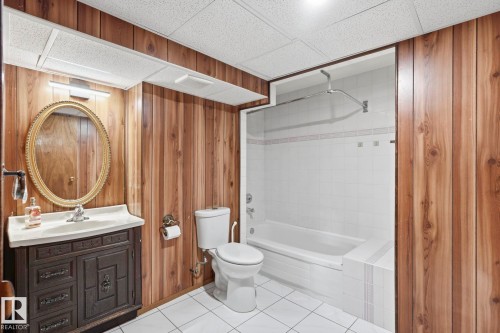Wood-paneled bathroom featuring a drop ceiling, white tiled flooring, a built-in bathtub with white tile surround, and a vanity with a mirror - 10007 168 Avenue Nw, Edmonton, AB - Indoor Photo Showing Bathroom