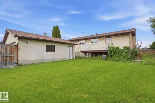 Expansive green lawn with a detached garage, wooden fence, and an elevated deck with white railings - 10007 168 Avenue Nw, Edmonton, AB - Outdoor With Exterior