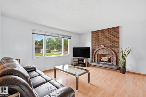 Living area featuring light wood-finish flooring, a prominent brick fireplace with an arched opening, and a large window providing ample natural light - 10007 168 Avenue Nw, Edmonton, AB - Indoor Photo Showing Living Room With Fireplace
