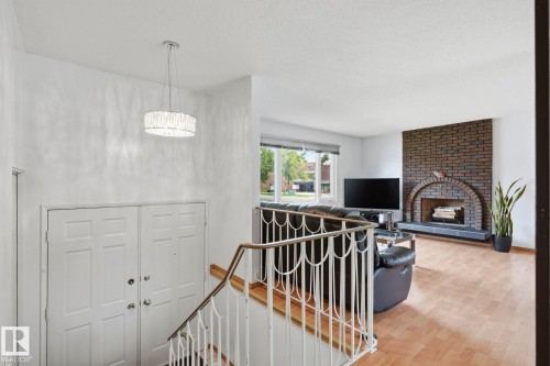 Hardwood-style flooring, brick fireplace with arched opening, large window with blinds, white paneled doors, and a decorative pendant light fixture - 10007 168 Avenue Nw, Edmonton, AB - Indoor With Fireplace