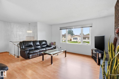Hardwood-finish flooring, white painted walls, large picture window, a partial brick-clad fireplace, and a contemporary chandelier fixture - 10007 168 Avenue Nw, Edmonton, AB - Indoor Photo Showing Living Room