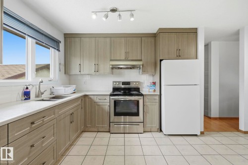 Kitchen featuring light wood-finish cabinetry, white tile flooring, stainless steel range, and a dual-basin sink - 10007 168 Avenue Nw, Edmonton, AB - Indoor Photo Showing Kitchen With Double Sink
