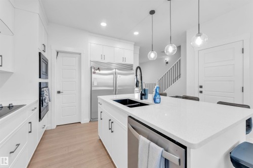 White cabinetry with contemporary hardware, stainless steel appliances, light wood-finish flooring, and pendant lighting - 3236 Chernowski Way Sw, Edmonton, AB - Indoor Photo Showing Kitchen With Double Sink With Upgraded Kitchen