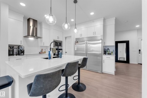 White shaker cabinetry, stainless steel appliances, central island with integrated sink, pendant lighting, and wood-finish flooring - 3236 Chernowski Way Sw, Edmonton, AB - Indoor Photo Showing Kitchen With Upgraded Kitchen