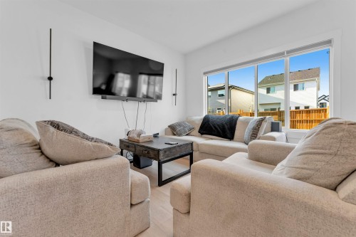 Large windows, hard-surface flooring, bright white walls, and contemporary wall-mounted lighting - 3236 Chernowski Way Sw, Edmonton, AB - Indoor Photo Showing Living Room