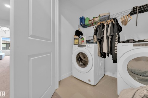 Laundry area featuring a front-loading washer and dryer, tile flooring, and integrated wire shelving - 3236 Chernowski Way Sw, Edmonton, AB - Indoor Photo Showing Laundry Room