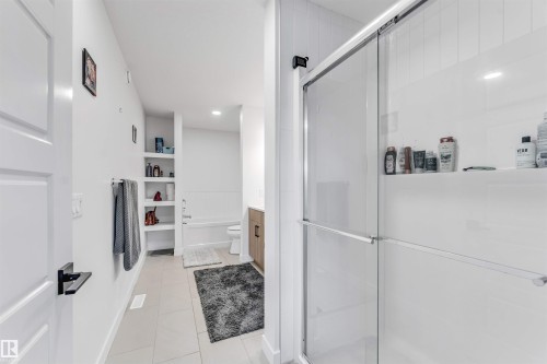 Glass-enclosed shower with white tiled walls, built-in recessed shelving, a separate bathtub, and tile flooring - 3236 Chernowski Way Sw, Edmonton, AB - Indoor Photo Showing Bathroom