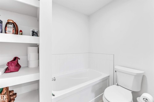 Built-in shelving, white ceramic toilet, white drop-in bathtub, and ceramic tile wainscoting - 3236 Chernowski Way Sw, Edmonton, AB - Indoor Photo Showing Bathroom