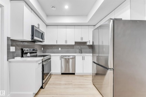 U-shaped kitchen with white cabinetry, light wood-finish flooring, stainless steel appliances, white countertops, and a gray subway tile backsplash - 3236 Chernowski Way Sw, Edmonton, AB - Indoor Photo Showing Kitchen With Upgraded Kitchen