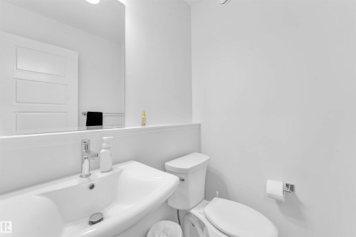 Pedestal sink with chrome faucet, wall-mounted mirror, white paneled door, and a wall-mounted toilet paper holder - 3236 Chernowski Way Sw, Edmonton, AB - Indoor Photo Showing Bathroom