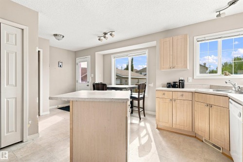 Kitchen island with light-toned cabinetry, light-colored countertops, and tile flooring - 204 84 Street Sw, Edmonton, AB - Indoor Photo Showing Kitchen With Double Sink