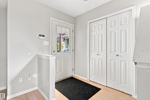 Entryway with light wood-finish flooring, a paneled door with glass inserts, and double bi-fold closet doors - 204 84 Street Sw, Edmonton, AB - Indoor Photo Showing Other Room