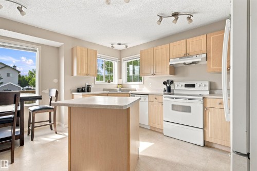 Light wood-finish cabinetry, solid surface countertops, white appliances, recessed lighting, and a center island - 204 84 Street Sw, Edmonton, AB - Indoor Photo Showing Kitchen With Double Sink