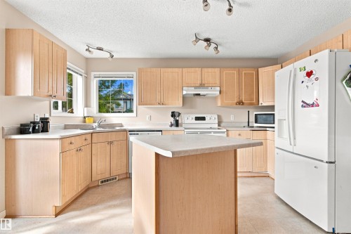 Kitchen featuring wood-finish cabinetry, track lighting, a central island, and white appliances - 204 84 Street Sw, Edmonton, AB - Indoor Photo Showing Kitchen With Double Sink