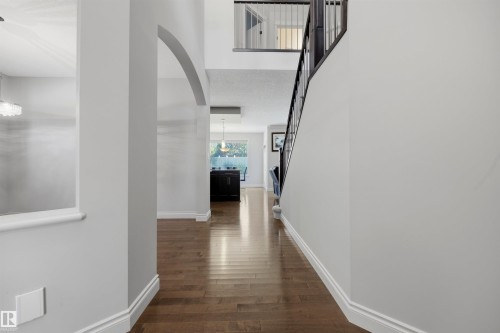 Spacious interior featuring wood-finish flooring, an elegant staircase with dark railings, a decorative arched doorway, and built-in display ledges - 2043 Cameron Ravine Way Nw, Edmonton, AB - Indoor Photo Showing Other Room