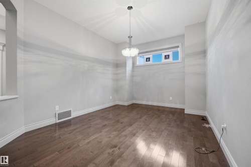 Spacious room featuring wood-finish flooring, light grey wall paint, and a contemporary pendant light fixture - 2043 Cameron Ravine Way Nw, Edmonton, AB - Indoor Photo Showing Other Room
