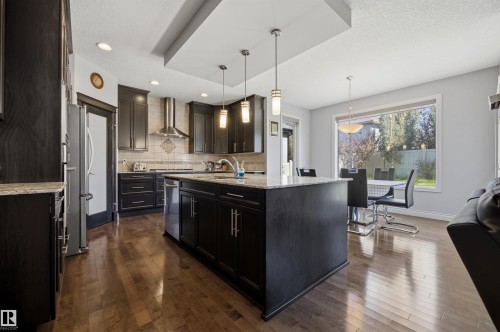 Kitchen featuring dark wood-finish cabinetry, stainless steel appliances, a central island with a light-toned countertop, and recessed lighting - 2043 Cameron Ravine Way Nw, Edmonton, AB - Indoor Photo Showing Kitchen With Upgraded Kitchen