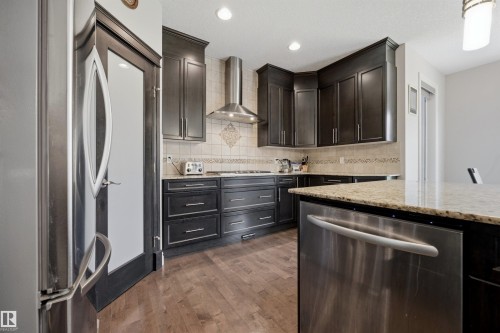 Full kitchen featuring dark wood cabinetry, light granite countertops, stainless steel appliances, and wood-finish flooring - 2043 Cameron Ravine Way Nw, Edmonton, AB - Indoor Photo Showing Kitchen With Upgraded Kitchen