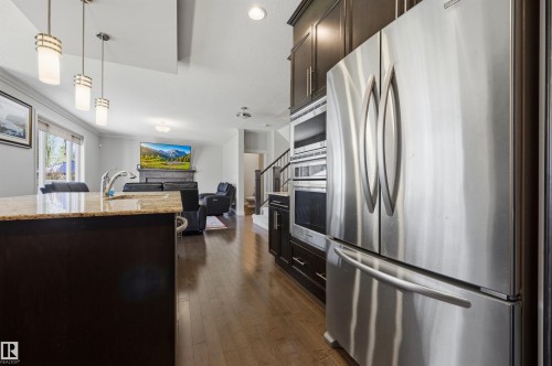 Stainless steel appliances, built-in microwave, wood-finish flooring, dark wood cabinetry, and a kitchen island with a stone-finish countertop - 2043 Cameron Ravine Way Nw, Edmonton, AB - Indoor Photo Showing Kitchen With Upgraded Kitchen