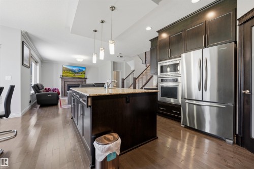 Kitchen island with a light-colored countertop, dark wood-finish cabinetry, and pendant lighting - 2043 Cameron Ravine Way Nw, Edmonton, AB - Indoor Photo Showing Kitchen With Upgraded Kitchen