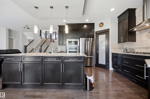Kitchen island with pendant lighting, dark wood-finish cabinetry, stainless steel appliances, and wood-finish flooring - 2043 Cameron Ravine Way Nw, Edmonton, AB - Indoor Photo Showing Kitchen With Upgraded Kitchen