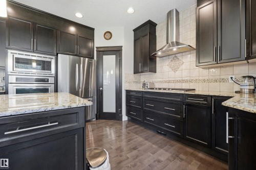 Kitchen featuring dark wood cabinetry, light-toned countertops, stainless steel appliances, and wood-finish flooring - 2043 Cameron Ravine Way Nw, Edmonton, AB - Indoor Photo Showing Kitchen With Upgraded Kitchen