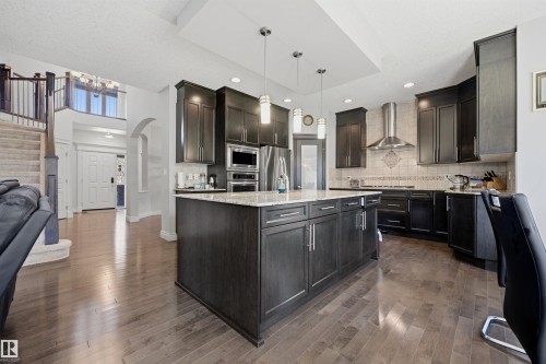 Open-concept kitchen featuring an oversized island with pendant lighting, dark wood-finish cabinetry, stainless steel appliances, and wood-finish flooring - 2043 Cameron Ravine Way Nw, Edmonton, AB - Indoor Photo Showing Kitchen With Upgraded Kitchen