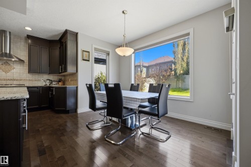 Kitchen featuring dark wood-finish cabinetry, stainless steel range hood, tile backsplash, and light-toned countertops - 2043 Cameron Ravine Way Nw, Edmonton, AB - Indoor Photo Showing Other Room