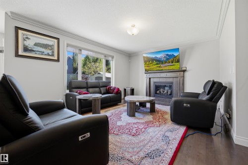 Spacious living area featuring large windows, wood-finish flooring, a built-in fireplace with a stone surround, and crown molding - 2043 Cameron Ravine Way Nw, Edmonton, AB - Indoor Photo Showing Living Room With Fireplace