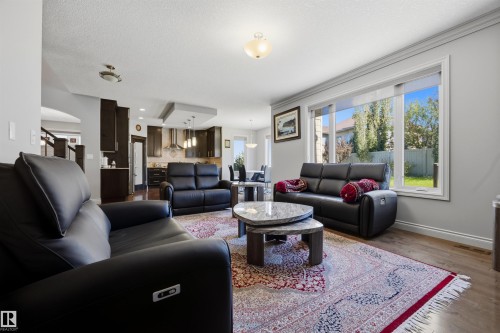 Open-concept living area with wood-finish flooring, a large window, and crown molding - 2043 Cameron Ravine Way Nw, Edmonton, AB - Indoor Photo Showing Living Room