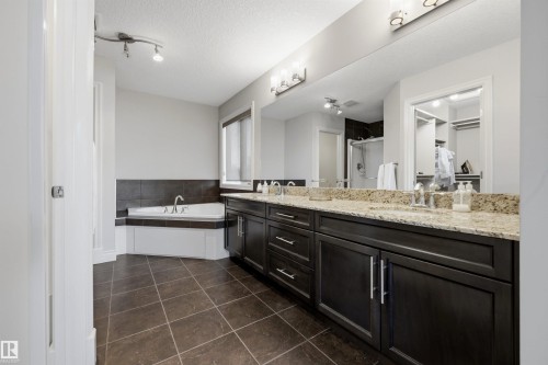 Corner soaking tub with tile surround, double vanity with stone-finish countertop, dark wood-finish cabinetry, and tiled flooring - 2043 Cameron Ravine Way Nw, Edmonton, AB - Indoor Photo Showing Bathroom