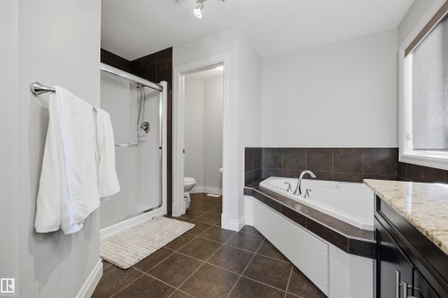 Built-in soaking tub with dark tile surround, separate shower with glass enclosure, track lighting, and a window with roller shade - 2043 Cameron Ravine Way Nw, Edmonton, AB - Indoor Photo Showing Bathroom