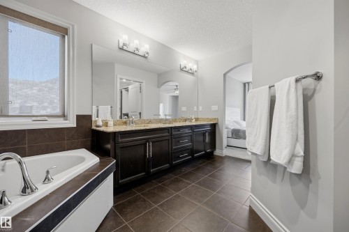 Dual vanity with stone countertop, large soaking tub, tiled flooring, and arched doorway - 2043 Cameron Ravine Way Nw, Edmonton, AB - Indoor Photo Showing Bathroom